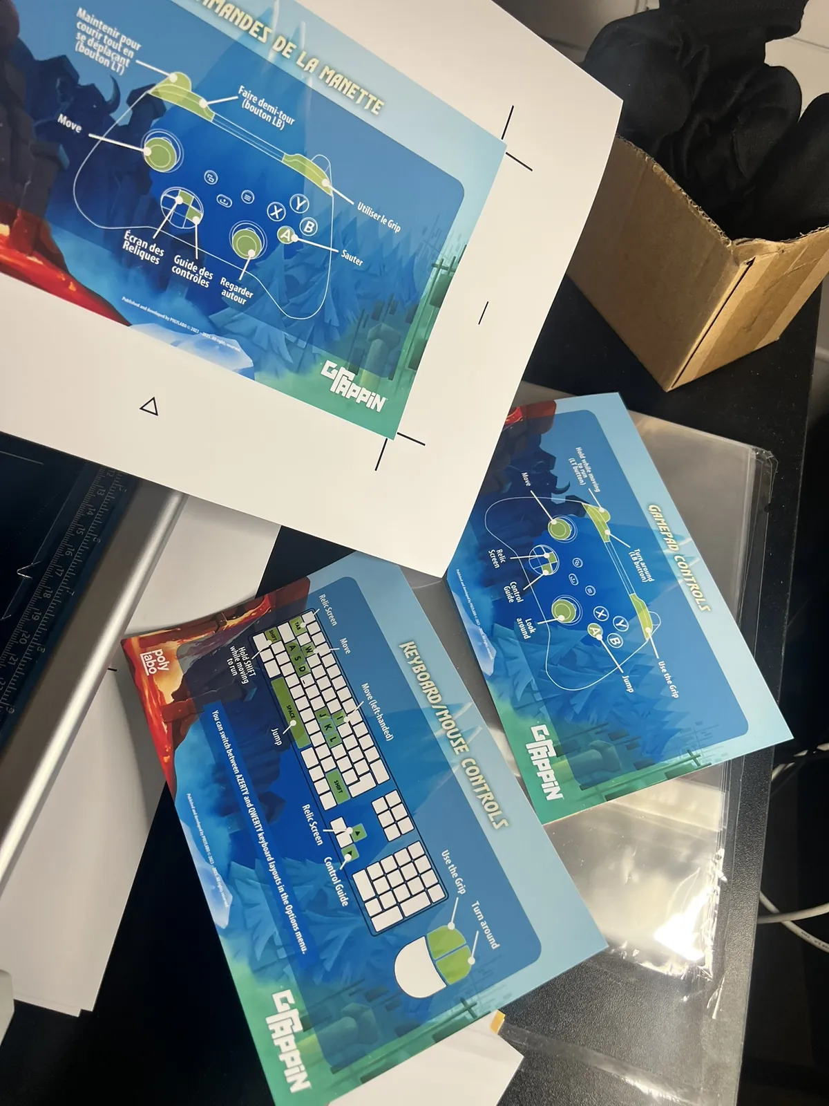Trimmed GRAPPIN control cards fanned out on the workbench showing gamepad and keyboard layouts.