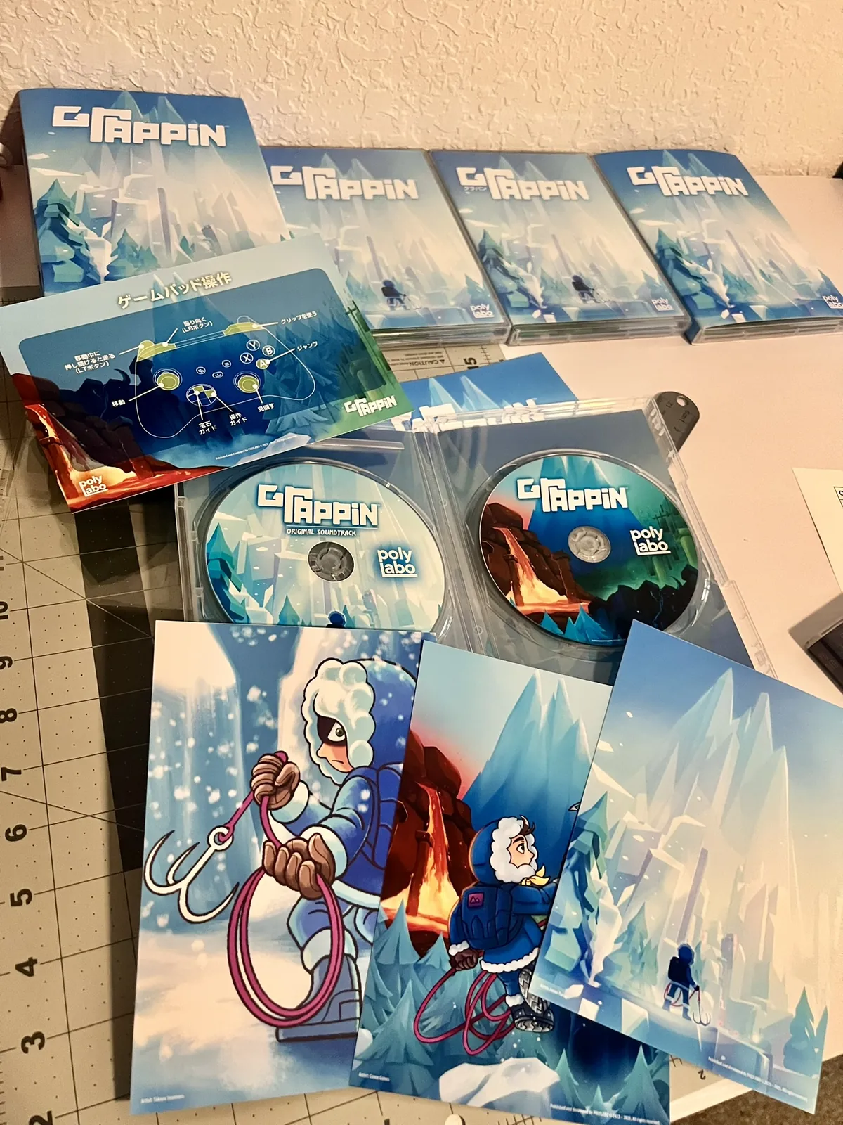 The full GRAPPIN deluxe edition laid out on a cutting mat: o-card sleeves, cases, the game and soundtrack discs, a controls card, and three art prints.