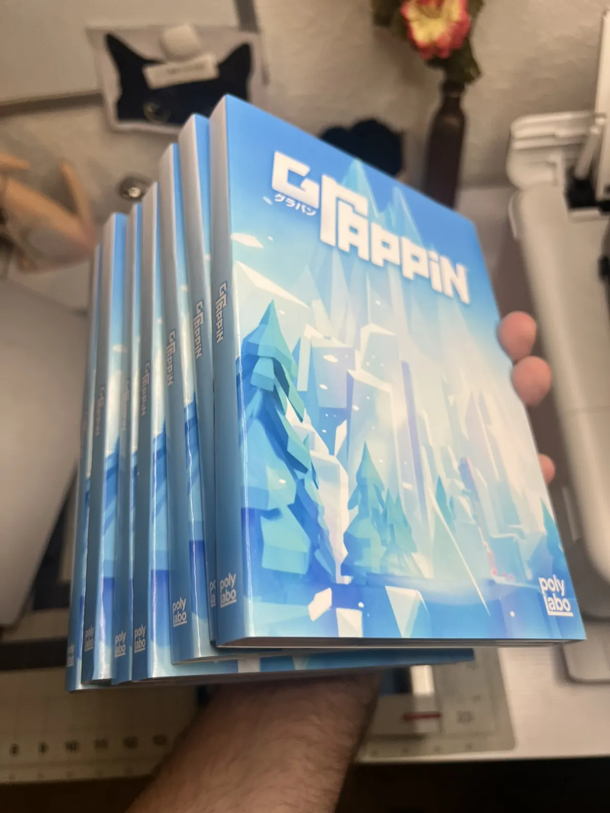A hand holding five finished GRAPPIN o-card editions fanned apart.