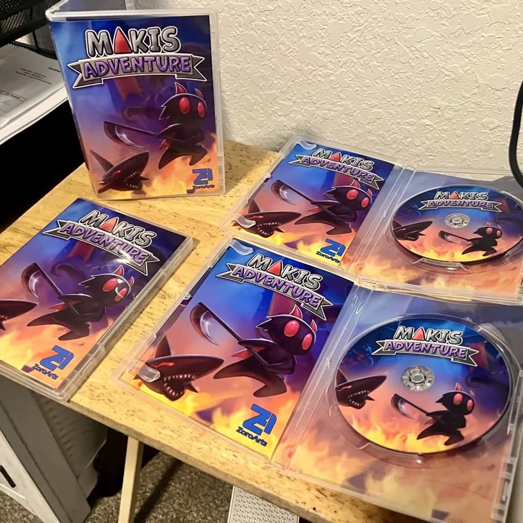 Five Maki's Adventure cases laid out on a table, two of them open to show the printed discs.